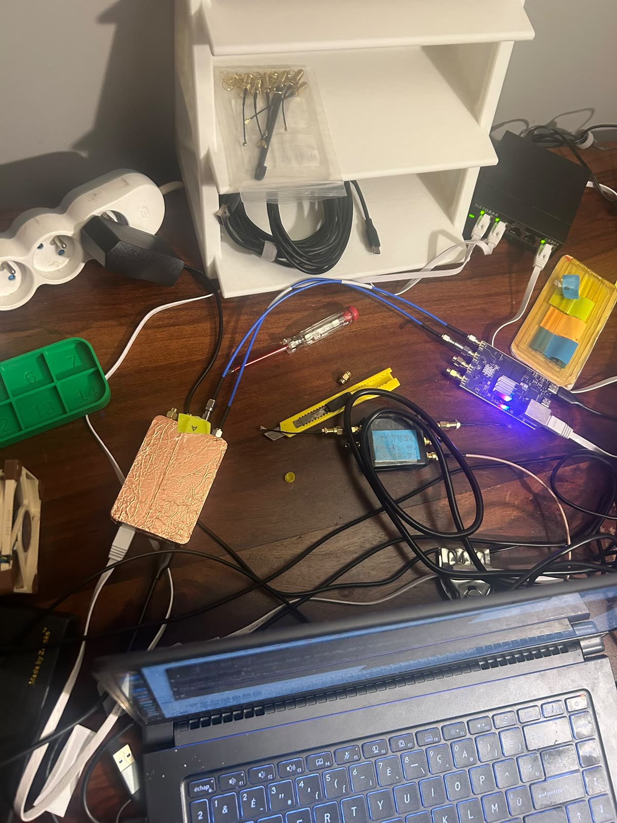 Le banc vu de haut : cartes SDR, câbles coaxiaux bleus, splitter, analyseur de spectre, et une carte enveloppée de cuivre
